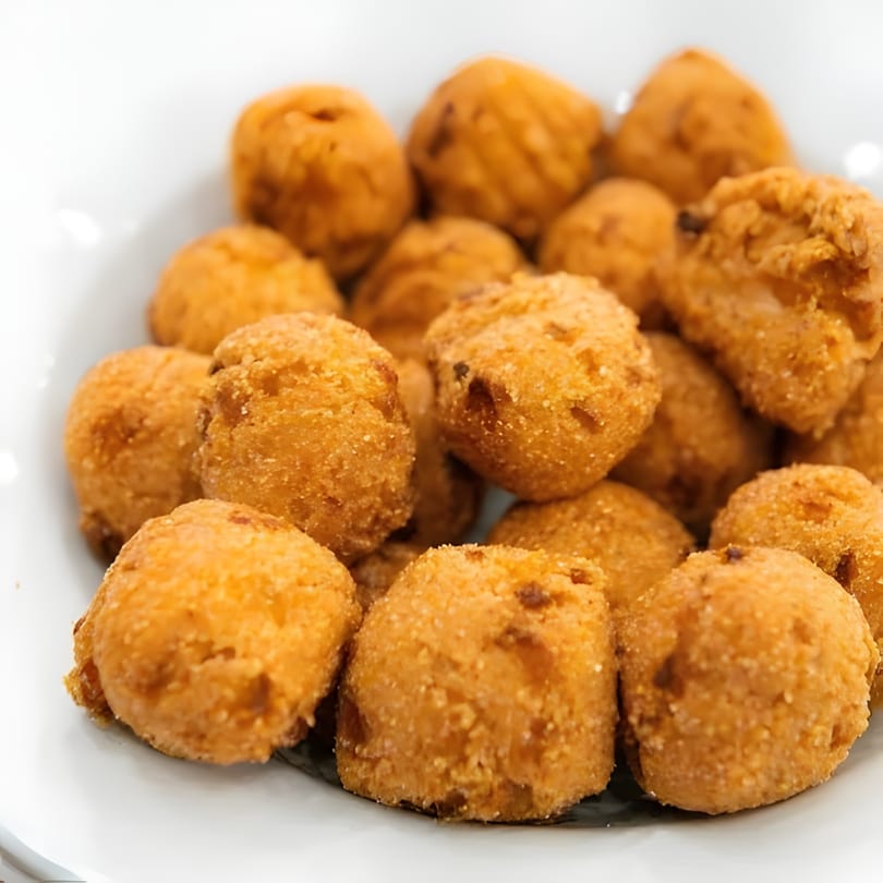 Close-up of a white bowl filled with golden-brown, crispy fried hushpuppies.
