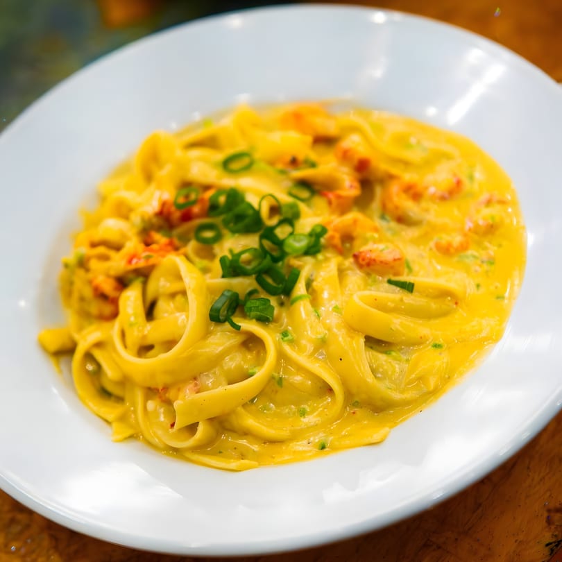 Creamy yellow fettuccine pasta with crawfish and green onions on a white plate.