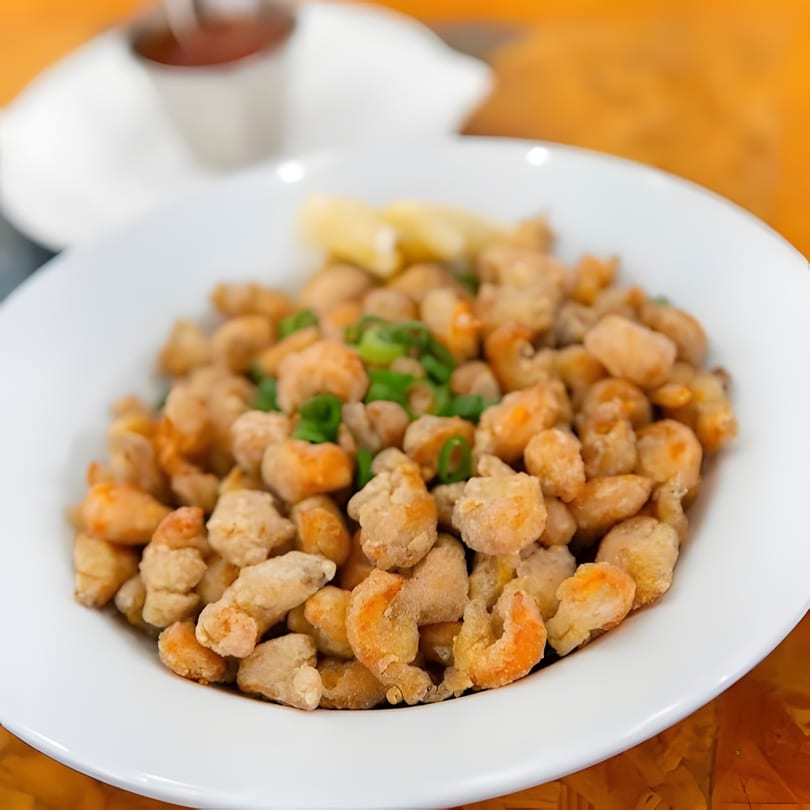 A white bowl filled with crispy fried popcorn shrimp, garnished with green onions and lemon wedges.
