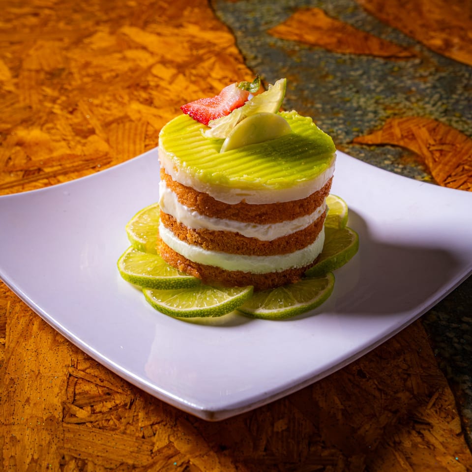 Layered lime dessert with creamy filling, avocado-colored topping, and fruit garnish on a white plate.
