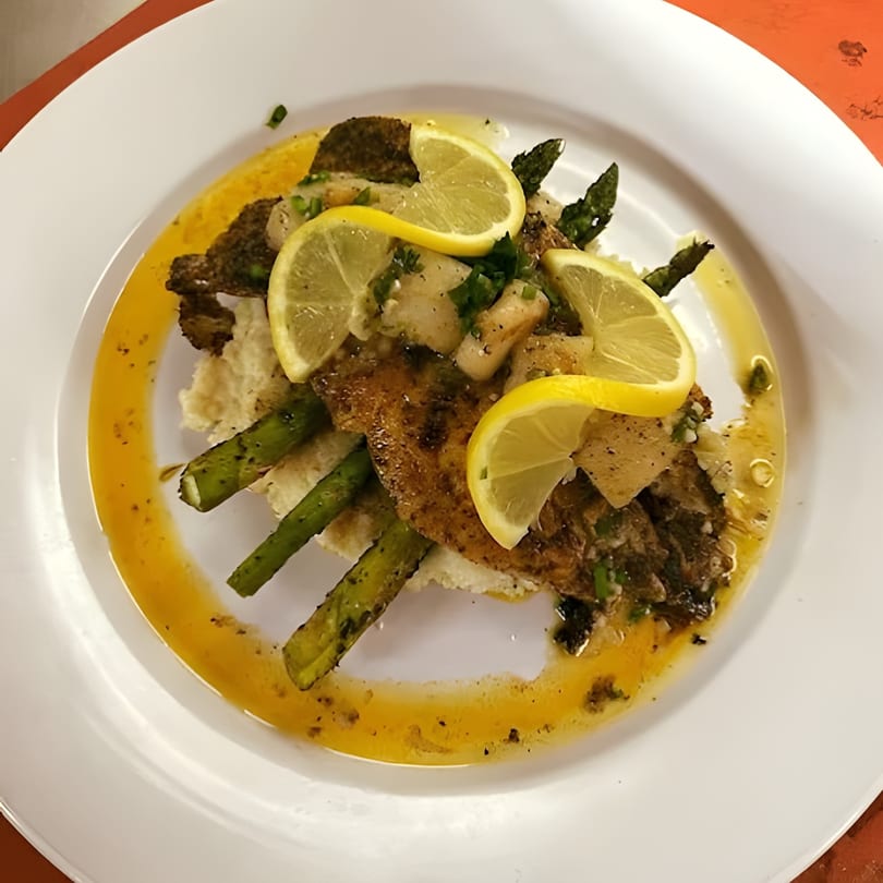 Pan-seared fish with asparagus, lemon slices, and a butter sauce on a white plate.