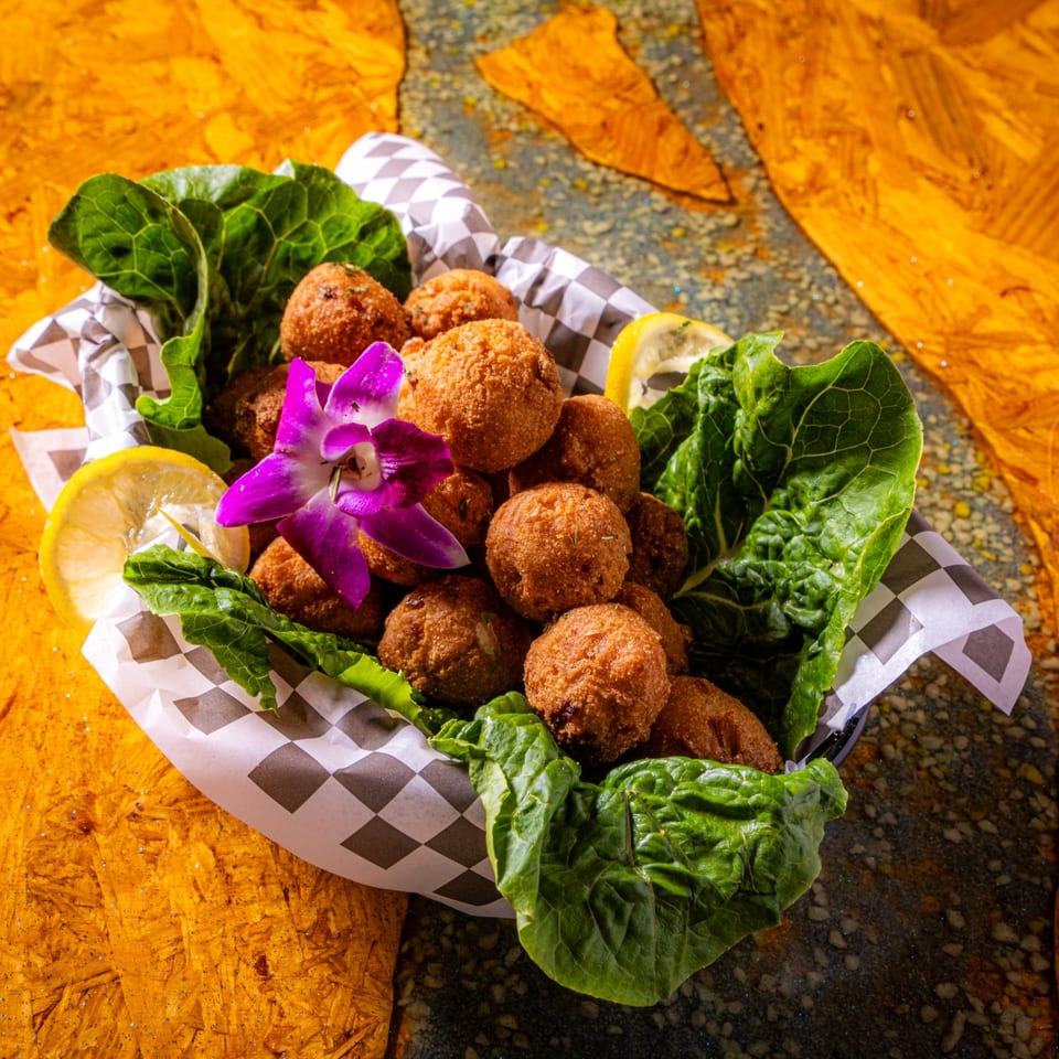 Basket of golden falafel balls garnished with lettuce, lemon slices, and a purple orchid on a wooden table.