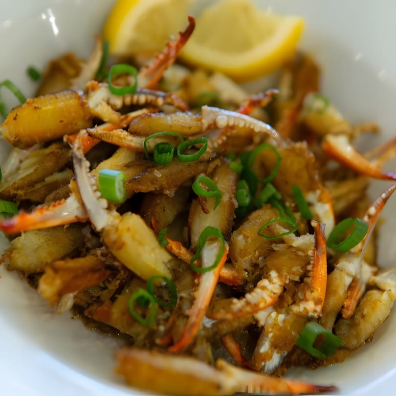 Close-up of fried crab claws and legs with green onions and lemon wedges in a white bowl.