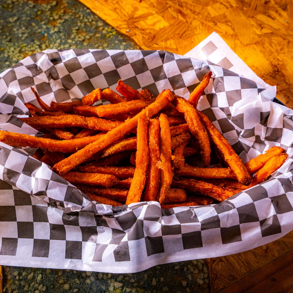 Basket of crispy golden sweet potato fries on black-and-white checkered paper atop a wooden table.